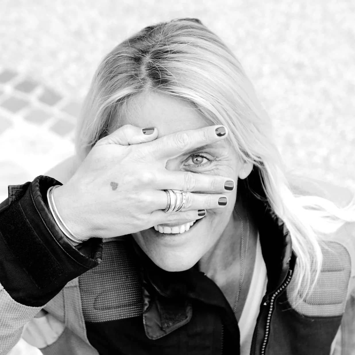 Tina Maria Werner lächelt und hält sich eine Hand vor ein Auge, schwarz-weiß